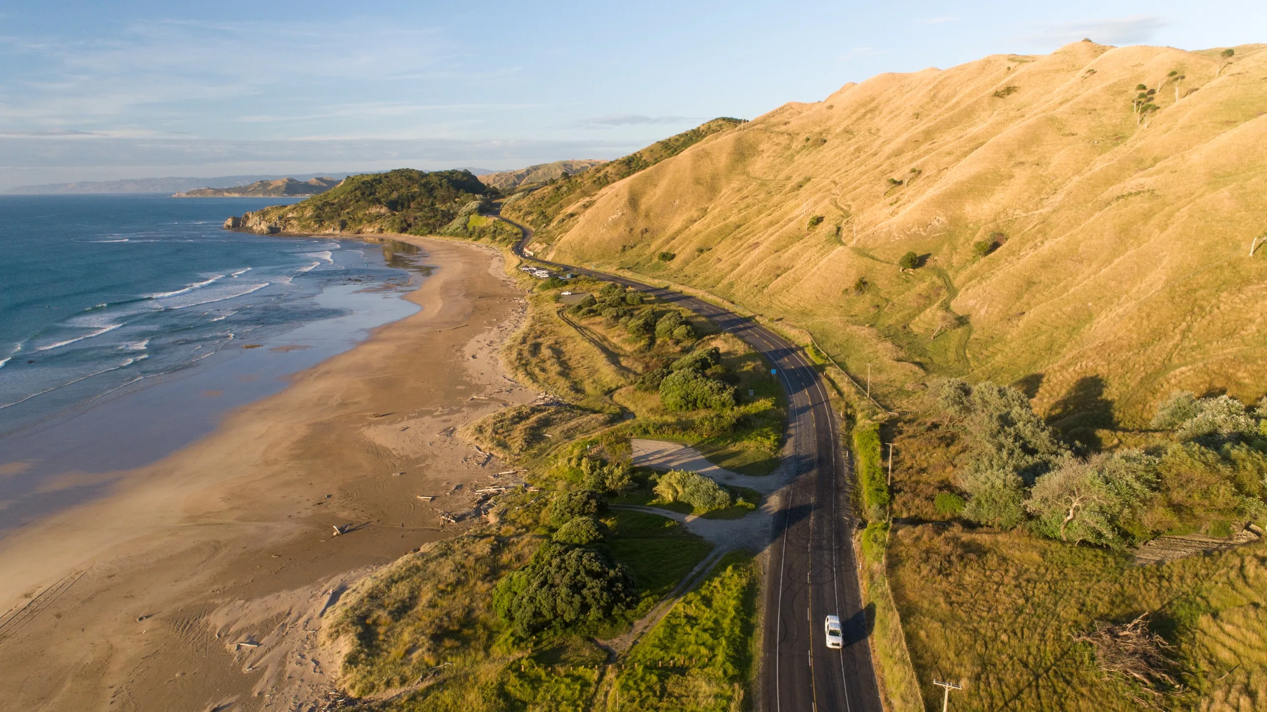 Aerial view of Mākōrori Beach with coastal road, golden hills and rolling surf